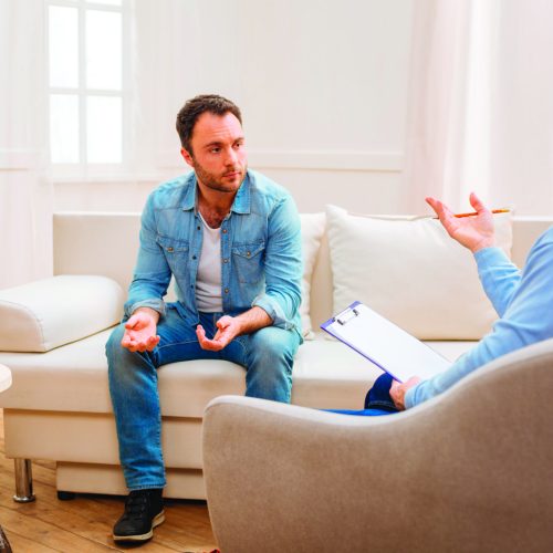 Psychologist advice. Lost upset unhappy man consulting with psychologist who sitting and holding folder and pencil